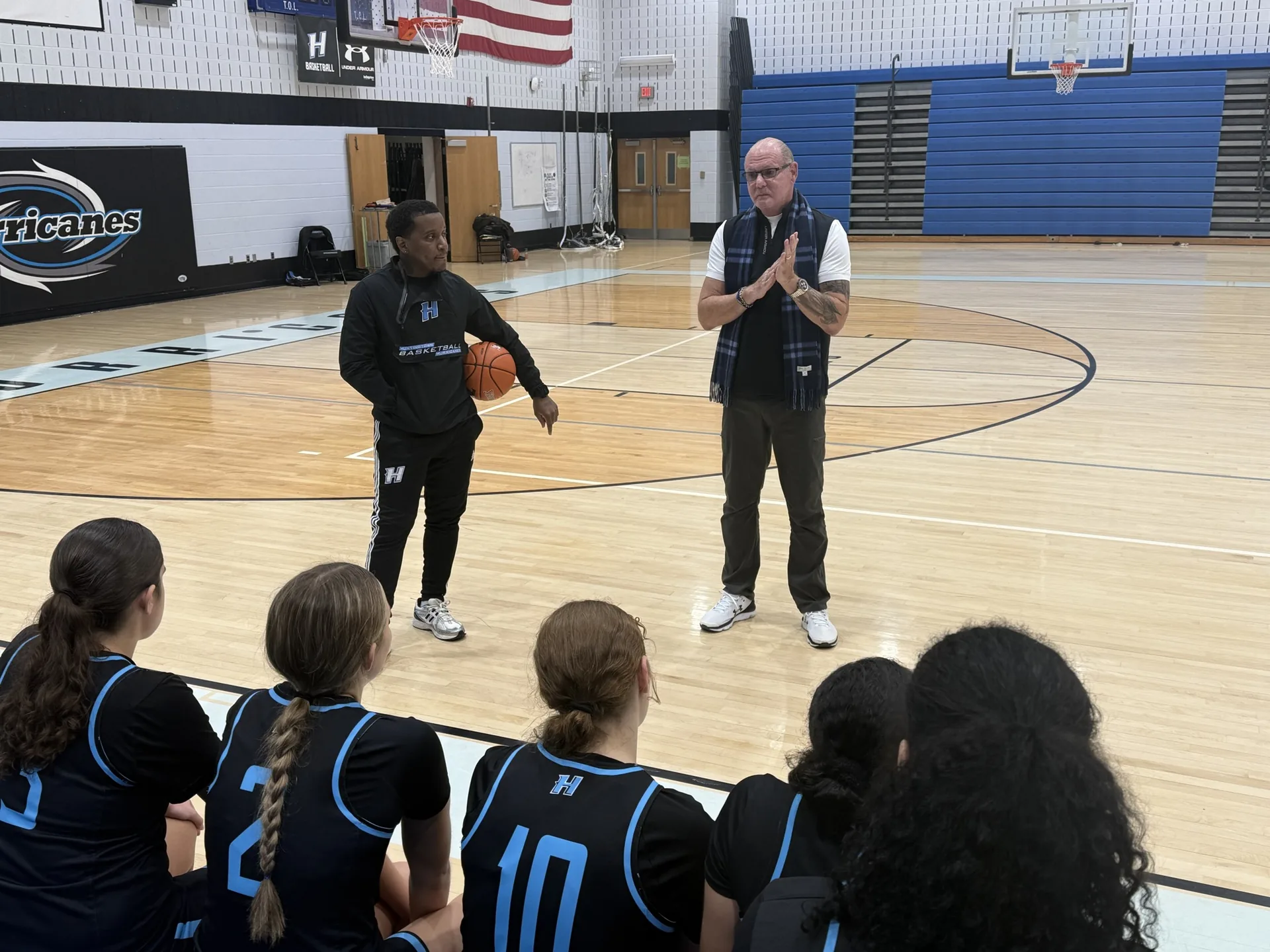 Donnie Downs speaking with a basketball team seated on a gymnasium court